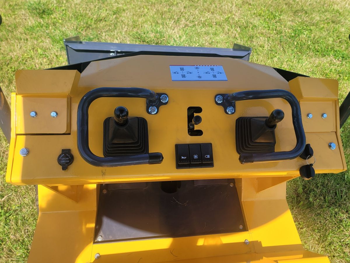 <p><strong>Hlavní ovládací prvky</strong> jsou umístěny přímo před obsluhou. Ochranné rámy hydraulických joysticků umožňují i jemné ovládání pojezdu a práci s ramenem.</p>
<p><strong>Trojice elektrických spínačů</strong> ovládá – klakson + ventilátor chladiče hydraulického oleje + pracovní LED světlo</p>